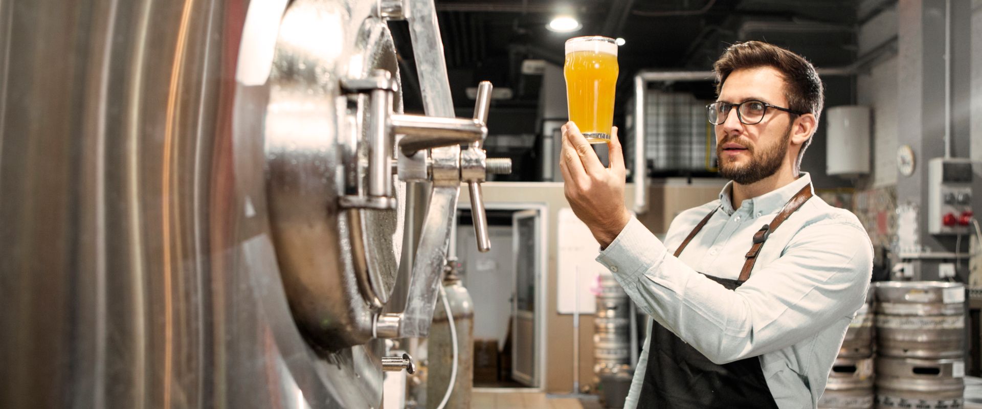 Man examining his craft beer in front of boiler for brewery